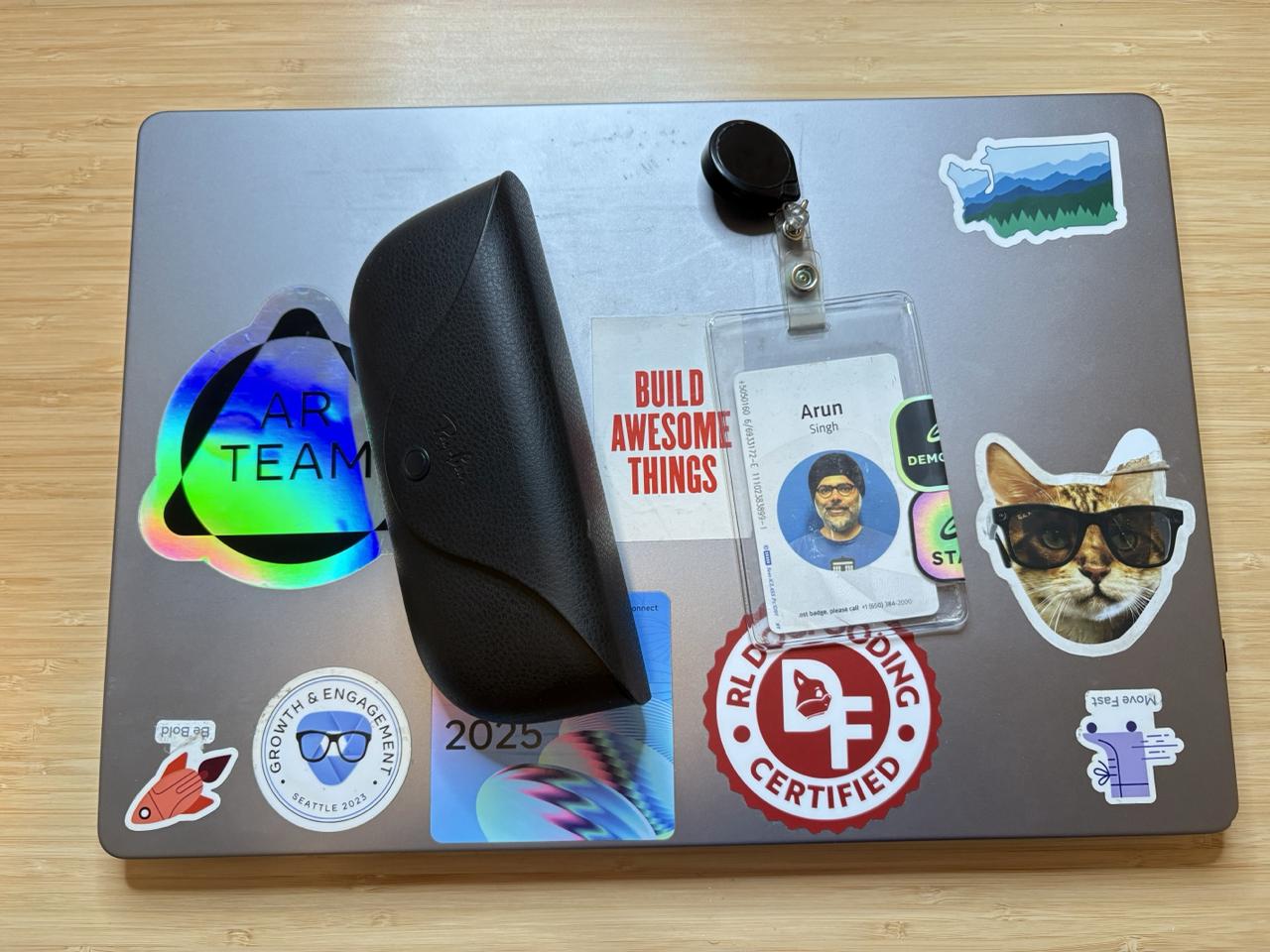 A laptop lid covered in stickers and badges collected over the years at Meta, with a clipped 'Arun Singh' ID badge resting on top